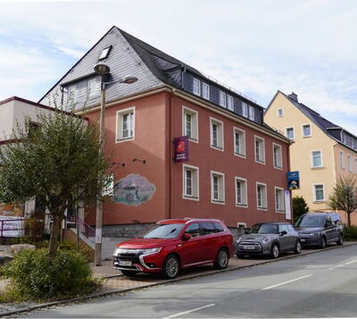 Mehrgeschossiges Wohn- und Geschäftshaus mit rotbrauner Fassade, Schieferdach und Wandmalerei an der Seitenwand